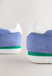 Sneakers in camoscio azzurro chiaro con dettagli bianchi e suola verde. Presentano una superficie testurizzata e dettagli di cucitura sul tallone.