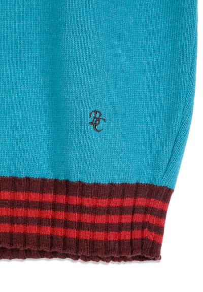Gros plan d'un tissu tricoté turquoise avec de petites lettres noires brodées et un ourlet côtelé à rayures marron et rouges.