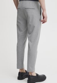 Grå sweatpants med en tapered design, elastisk talje og to baglommer. Båret med sorte slip-on sko. Glat tekstur.