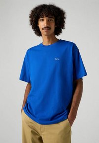 Camiseta de algodón azul con mangas cortas, que presenta un pequeño bordado blanco de "París" en el pecho. Color sólido con un corte relajado.