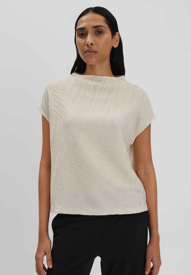 Top corto a maniche corte di un beige chiaro con un motivo testurizzato a zigzag. Il collo rotondo e la vestibilità ampia creano una silhouette rilassata.