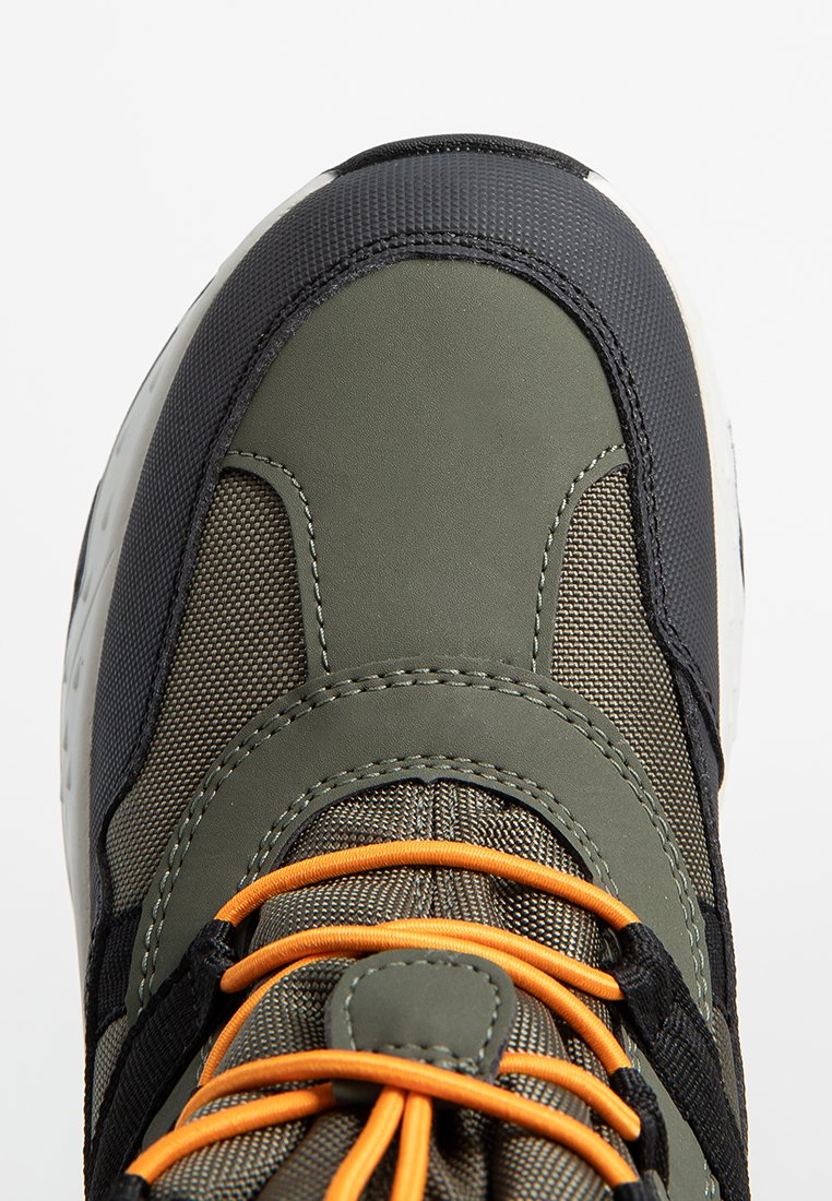 Grüner und schwarzer Sport Schuh mit einer strukturierten Oberseite, orangefarbenen Schnürsenkeln und einer gepolsterten Sohle mit Gummielementen.