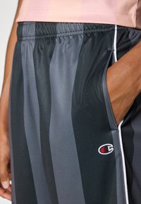 Pantalones cortos deportivos en negro y gris con un diseño a rayas, cintura elástica, bolsillo lateral y logo bordado en la pierna izquierda.