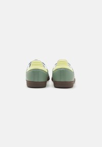 Green and yellow sneakers featuring a smooth synthetic upper, textured accents, and a brown rubber sole with a patterned tread.