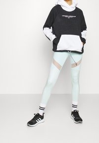 Sudadera en blanco y negro con un bolsillo delantero, combinada con leggings azul claro que tienen paneles translúcidos, y zapatos negros con detalles en blanco.