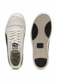 Hvide lædersneakers med sorte accenter, perforeret tå, flade snørebånd og en tekstureret gummisål med bølge mønster og logodetalje.