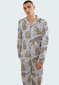 Conjunto de pijama a rayas azules con un estampado de leopardo repetido. El material es suave; el diseño incluye una camisa de botones y pantalones a juego.
