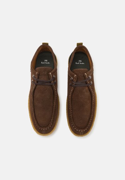 Brown suede shoes with a rounded toe, tan rubber sole, and contrasting white stitching. Features laces and a branded black insole.