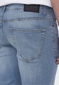Ljusblå jeans i denim med en bakficka som har en kurvad design och en svart tygetikett med texten "ONLY & SONS" vid midjan.