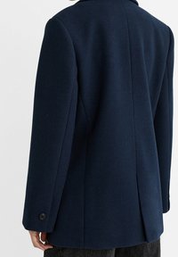 Abrigo de lana azul marino con diseño entallado, una sola abertura trasera y puños abotonados, que muestra una textura suave y una silueta clásica.