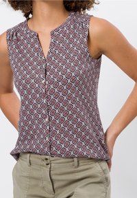Blouse sans manches avec un motif floral dans des teintes de rouge, blanc et bleu marine. Encolure en goutte d'eau et fermeture à boutons sur le devant. Tissu léger.