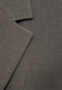 Tissu gris foncé avec une fine texture de tissage diagonal, montrant les revers qui se chevauchent d'une veste ou d'un blazer sur mesure.