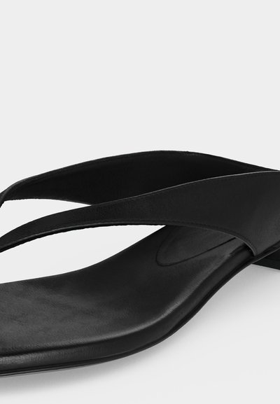 Μαύρο δερμάτινο σανδάλι με τετράγωνη μύτη και φαρδιές διασταυρούμενες λουρίδες, εμφανιζόμενο από κοντινή πλευρική γωνία.