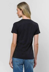 Melnas īsām piedurknēm T-krekls, kas izgatavots no mīksta kokvilnas auduma, ar apaļu kakla izgriezumu un taisnu apakšmalu. Valkāts kopā ar gaiši ziliem džinsiem.