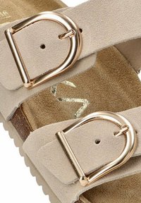 Sandalia de ante beige con dos cintas anchas, con hebillas de metal en tono dorado, plantilla texturizada y suela de madera marrón.