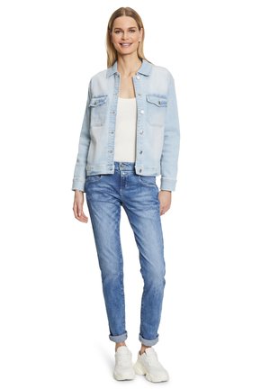 Light blue denim jacket with two chest pockets, worn over a white tank top. Paired with light blue rolled-up jeans and white sneakers.