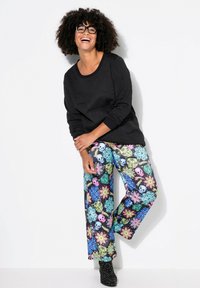 Maglietta nera a maniche lunghe con collo a girocollo, abbinata a pantaloni larghi e colorati con motivi di fiori e teschi.