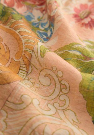 Floral fabric featuring a textured design of pink and green leaves, orange swirls, and blue flowers on a soft, peach background.