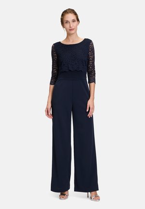 Navy jumpsuit with lace three-quarter sleeves, a fitted lace bodice, pleated waist, and wide-leg trousers. Smooth texture with elegant design.