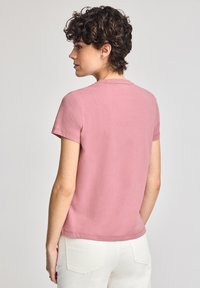 Camiseta de manga corta y cuello redondo en suave algodón rosa empolvado. Diseño minimalista con una forma ligeramente ajustada y espalda lisa.