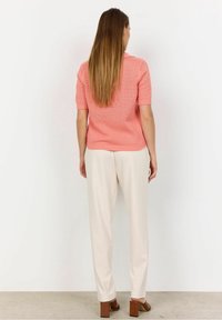 Vaaleanpunainen neulottu toppi lyhyillä hihoilla, teksturoitu kuvio, yhdistettynä kermaisiin housuihin ja ruskeisiin palleakorkoisiin kenkiin.