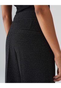 Pantalon noir à motifs avec un tissu texturé, des détails de couture visibles et une poche arrière unique. Coupe ajustée avec une conception à jambe droite.