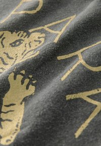 Un tissu gris au toucher doux présente un graphique de tigre doré bien en vue et des lettres audacieuses, créant un contraste visuel saisissant.