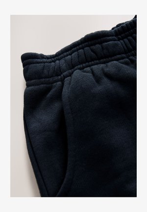 Čierne bavlnené teplákové nohavice s rebrovaným pásom, bočnými vreckami a mäkkou, česanou textúrou. Tkanina má mierne štruktúrovaný vzhľad.