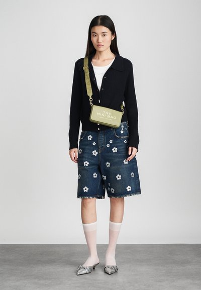 Μαύρο ραμμένο cardigan, τζιν σορτς με λευκή floral κεντητική, ελκυστική πράσινη τσάντα χιαστί, ασημένια μυτερά παπούτσια, λευκές κάλτσες μέχρι το γόνατο.