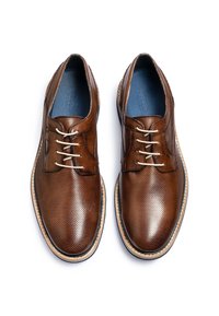 Scarpe in pelle marrone con superficie texturizzata, caratterizzate da dettagli cuciti e cinque occhielli. Suola in gomma con un bordo chiaro a contrasto.