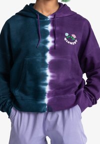 Sudadera con capucha con un diseño degradado en verde azulado y púrpura. Cuenta con un bolsillo tipo canguro y bordado floral en el pecho. Textura suave.