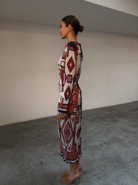 Robe maxi avec des motifs géométriques en rouge, blanc et marron, dotée d'un corsage ajusté et d'une jupe évasée. Accentuée par un ourlet festonné.