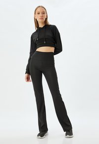 Zwart sportset bestaande uit een cropped hoodie met trekkoord en high-waisted flare leggings. Glad stof met een getailleerd ontwerp.