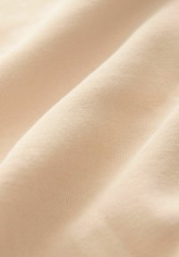 Tissu beige clair avec une texture lisse, présentant des nervures horizontales subtiles et des plis, indiquant un tombé et une douceur.
