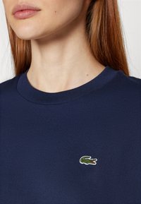 Navy blue cotton t-shirt with a round neckline and a small embroidered crocodile logo on the chest. Smooth texture and classic fit.