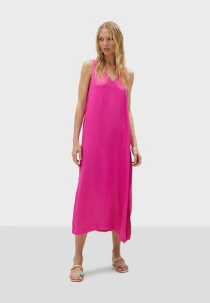 Robe maxi sans manches rose en tissu léger, avec un décolleté en V et une fente latérale. Portée avec des sandales décoratives.