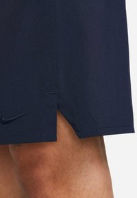Navy athletic shorts with a smooth texture and side slits. Features a discreet Nike logo embroidered in dark thread on the lower hem.