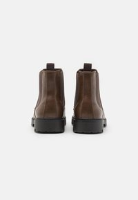 Botas de tobillo de cuero marrón con paneles elásticos en los laterales, tiradores y suelas de goma negra. Acabado suave con detalles de costura visibles.