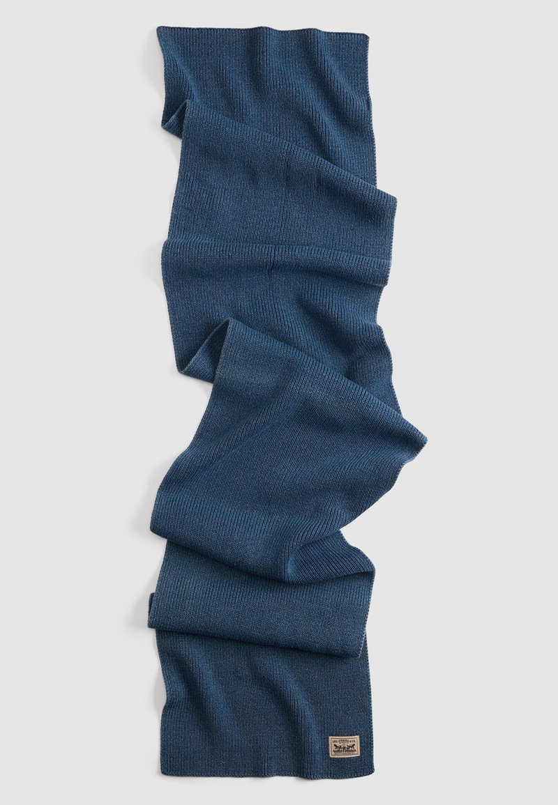 Strikkscarf i dyb marineblå farve, med et struktureret mønster og et lille, rektangulært brandmærke i bunden.