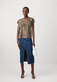 Top a maniche corte con stampa leopardata abbinato a una gonna in denim scuro con spacco frontale. Gli accessori includono una borsa bianca e tacchi trasparenti.