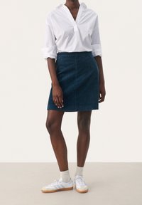 Falda de mezclilla en terracota azul oscuro con corte recto, combinada con una camisa blanca de cuello y zapatillas blancas con suelas de goma.