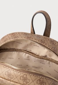 Zaino marrone con motivo e superficie testurizzata. L'interno presenta una fodera beige con il logo 'GUESS' ripetuto. Chiusura con zip e tirante.