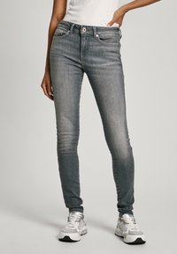 Slim-fit, středně vysoké šedé džíny s jemným opotřebením, pěti kapsami a knoflíkovým zapínáním. V kombinaci s bílými teniskami pro kontrast.