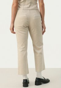 Beige ribfluwelen broek met een slim fit, voorzien van een rechte pijp, twee achterzakken en subtiele verticale strepen. G gedragen met zwarte schoenen en witte sokken.