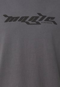 Camiseta de algodón gris con un gran logo negro impreso "magic" en el frente, de textura suave y corte casual.