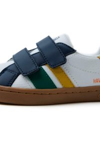 Zapatilla blanca con tiras de velcro azules, rayas verdes y amarillas, y una suela de goma marrón. Presenta un material de cuero texturizado y una marca.