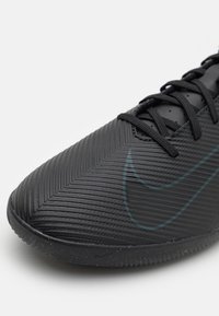 Svart atletisk sko med en texturerad herringbone-mönster ovandel, med en subtil mörk teal Nike-swoosh och svarta snören.