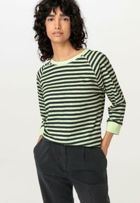 Schwarz und hellgrün gestreiftes Langarmshirt mit Rundhalsausschnitt und Raglanärmeln, aus weichem Stoff, kombiniert mit dunklen Hosen.