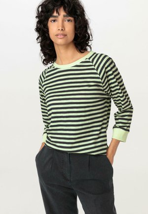 Schwarz und hellgrün gestreiftes Langarmshirt mit Rundhalsausschnitt und Raglanärmeln, aus weichem Stoff, kombiniert mit dunklen Hosen.