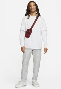 Witte oversized t-shirt over een lange mouw witte blouse, gecombineerd met lichtgrijze cargo pants en witte sneakers. Rode crossbody tas.
